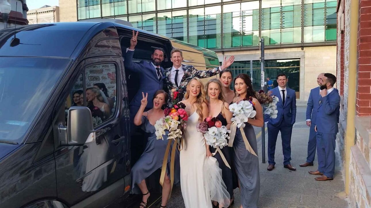 Bride, bridesmaids, and groomsmen posing by a wedding van.