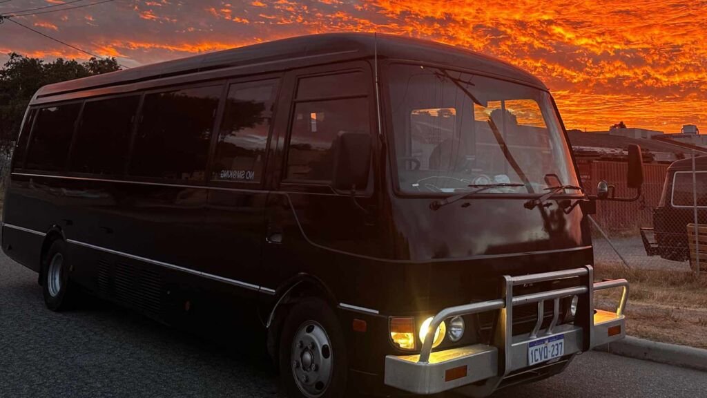 The West Coast Boogie Bus, a black bus parked on a street against a vibrant, fiery orange sunset sky.