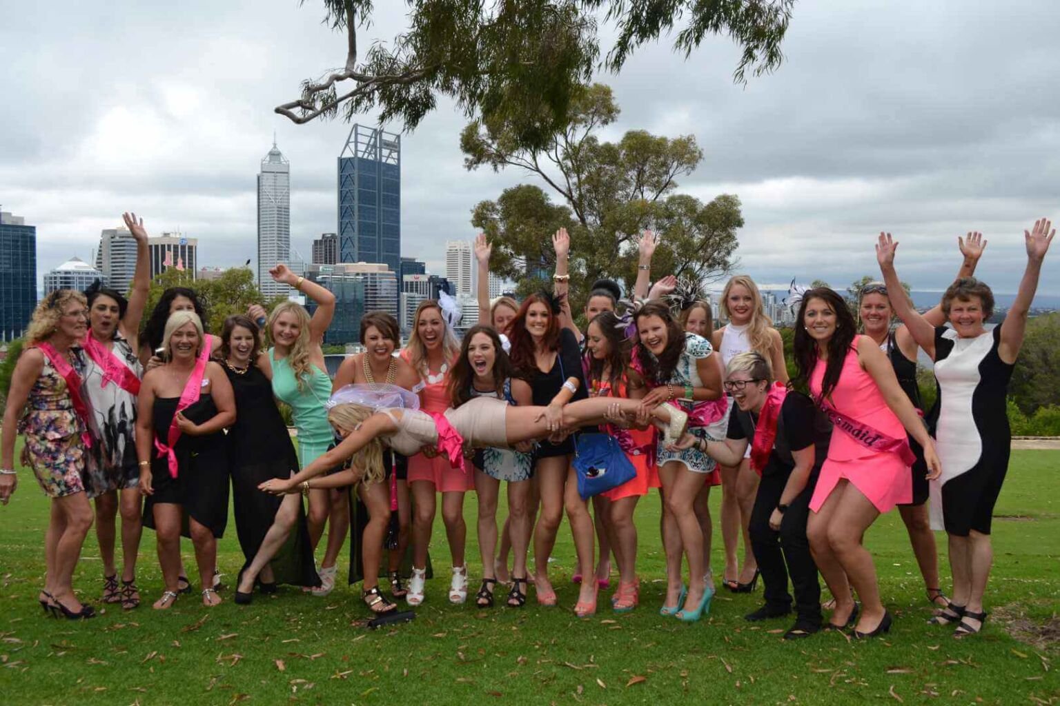 A group of women joyfully pose on grass during a hen party.