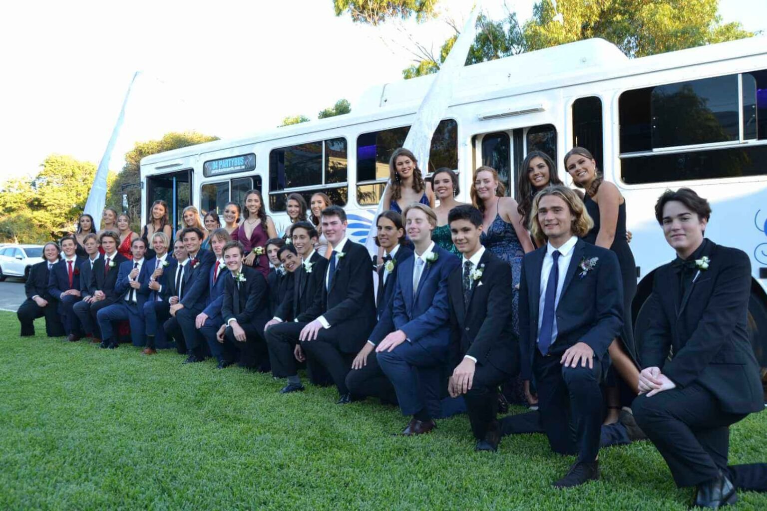 Prom group posing in front of a white party bus.