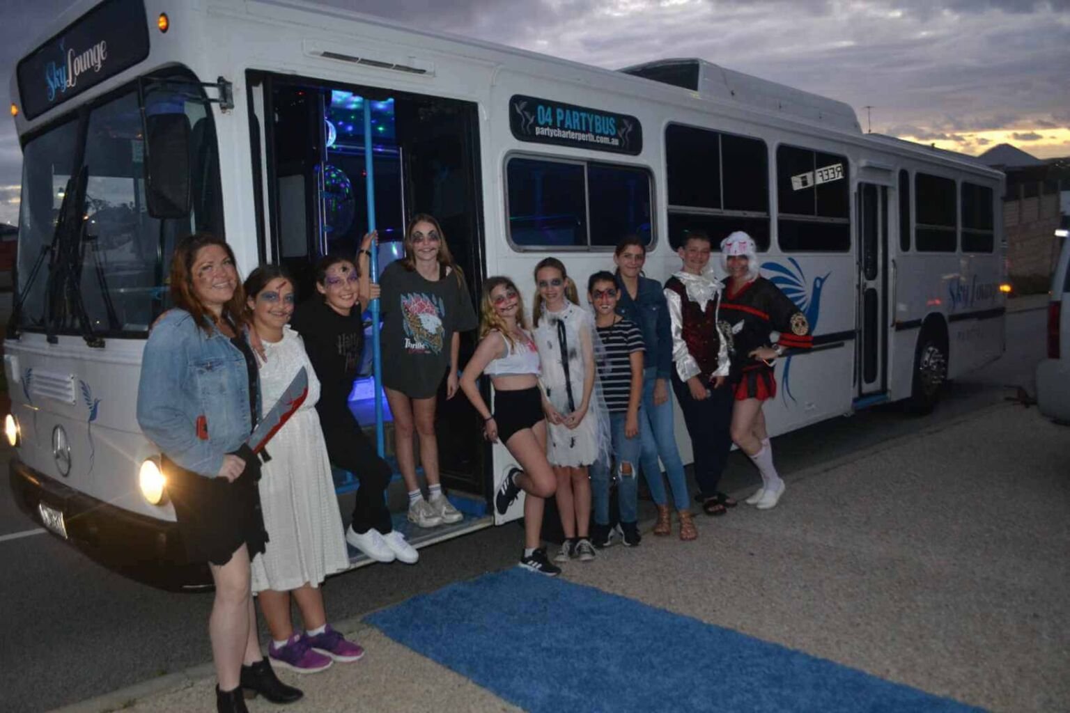 A group of children celebrating a birthday posing in front of a party bus labeled Sky Lounge.