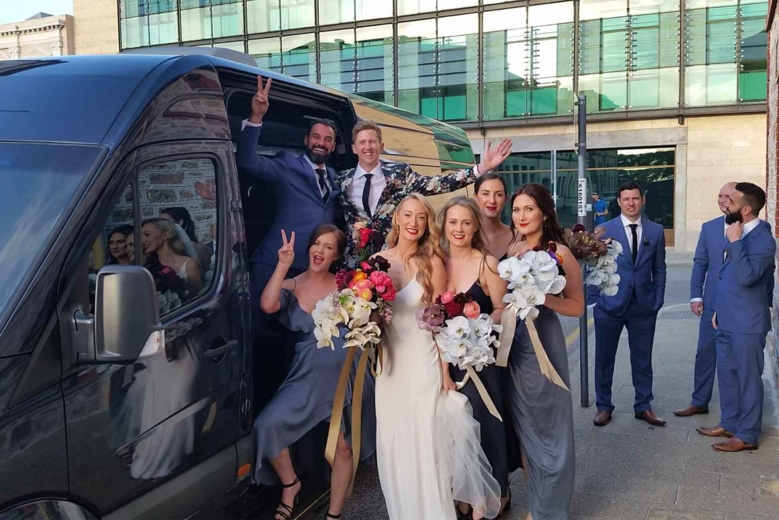 Bride, bridesmaids, and groomsmen posing by a wedding van.