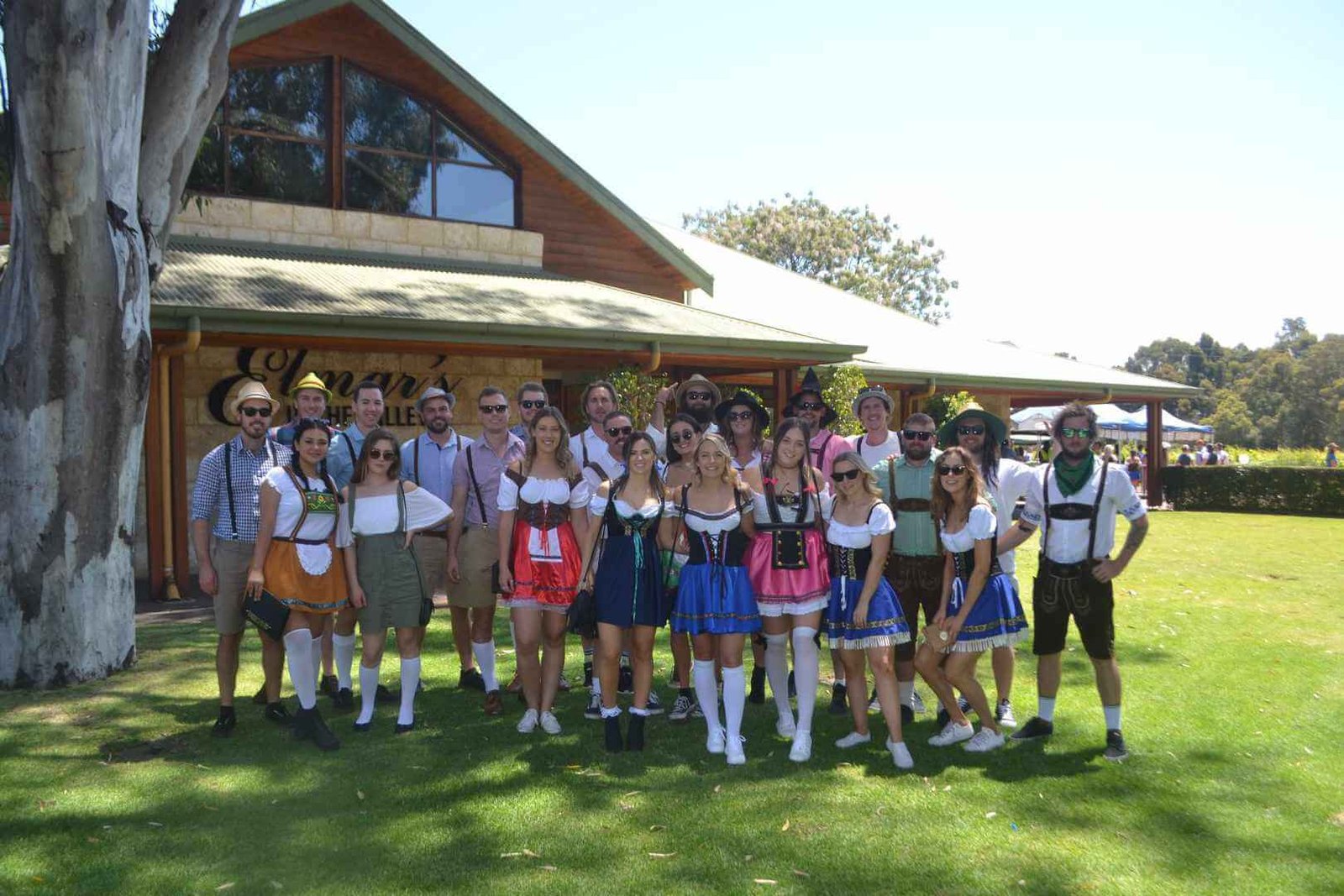 A group of people in traditional Bavarian costumes poses cheerfully on a grassy lawn during a wine tour.
